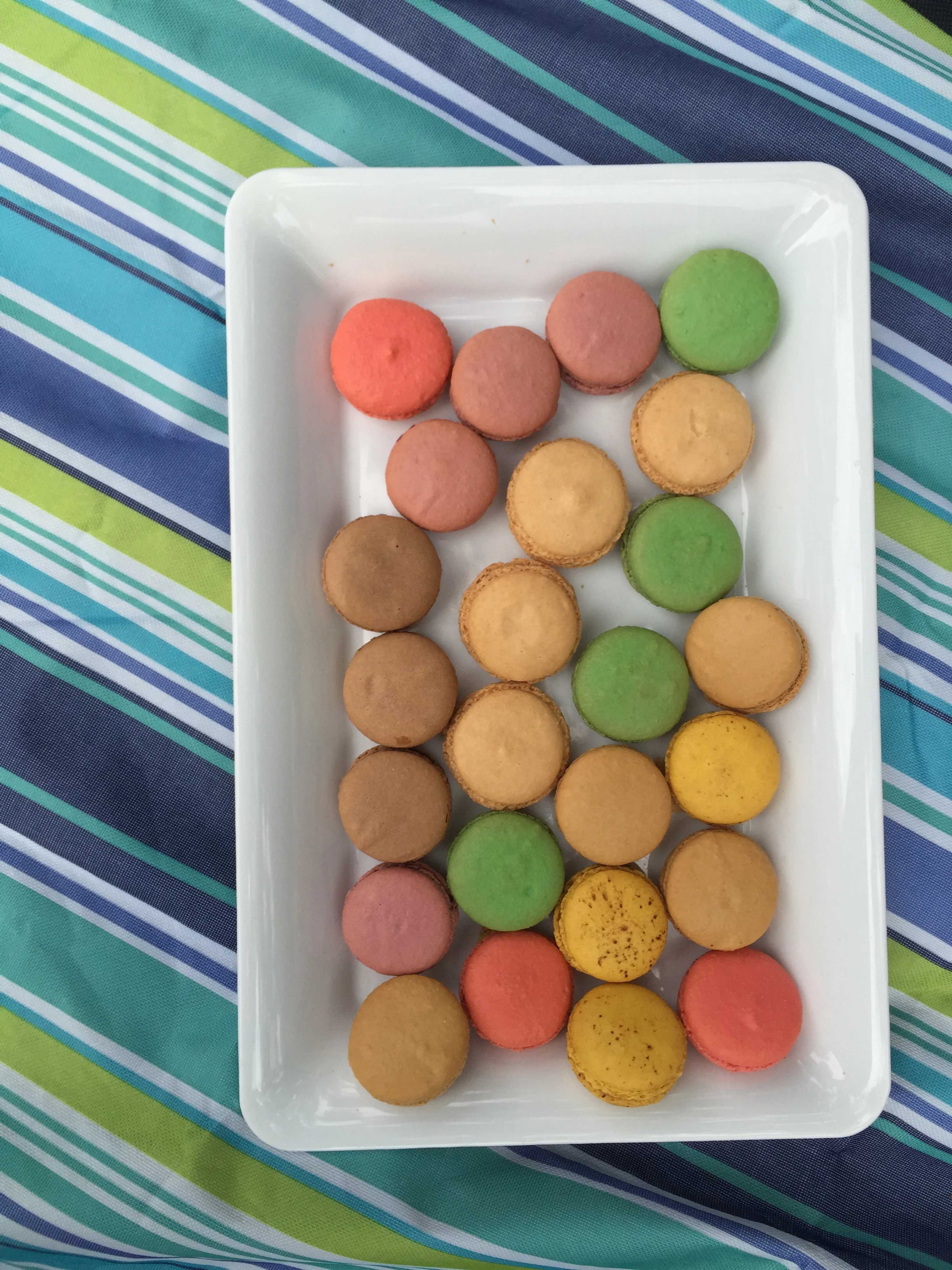 Overhead shot of a white tray of pastel macarons in pink, pistachio green, lemon yellow and cocoa brown, soft daylight palette
