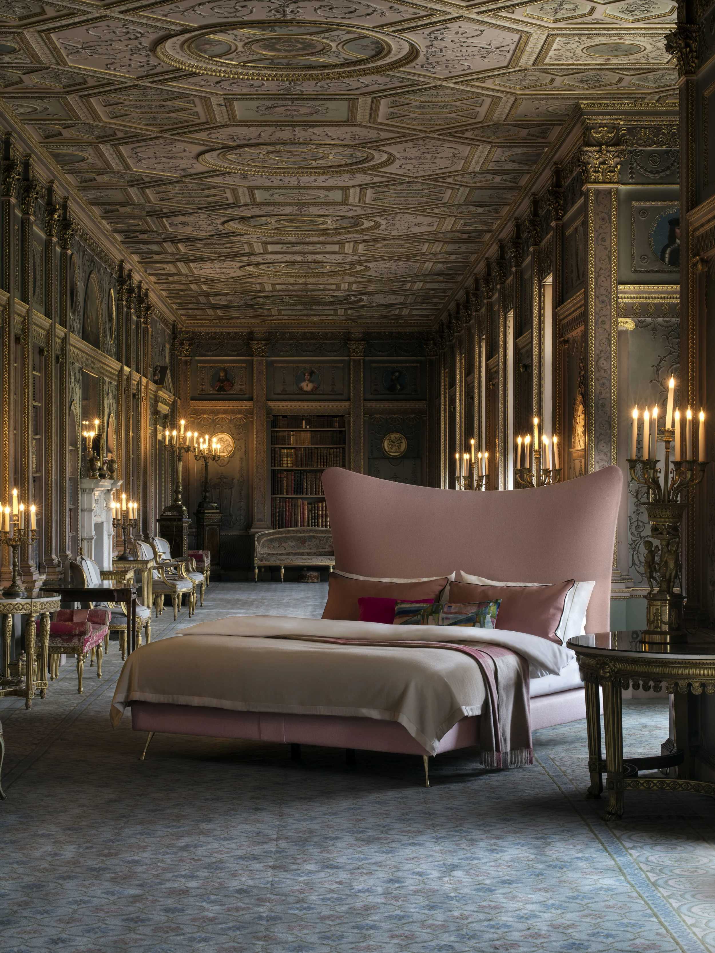 Ornate historic gallery with a gilded coffered ceiling, lit candelabras, tall bookshelves and a patterned marble floor, bathed in soft warm light with a modern pink accent